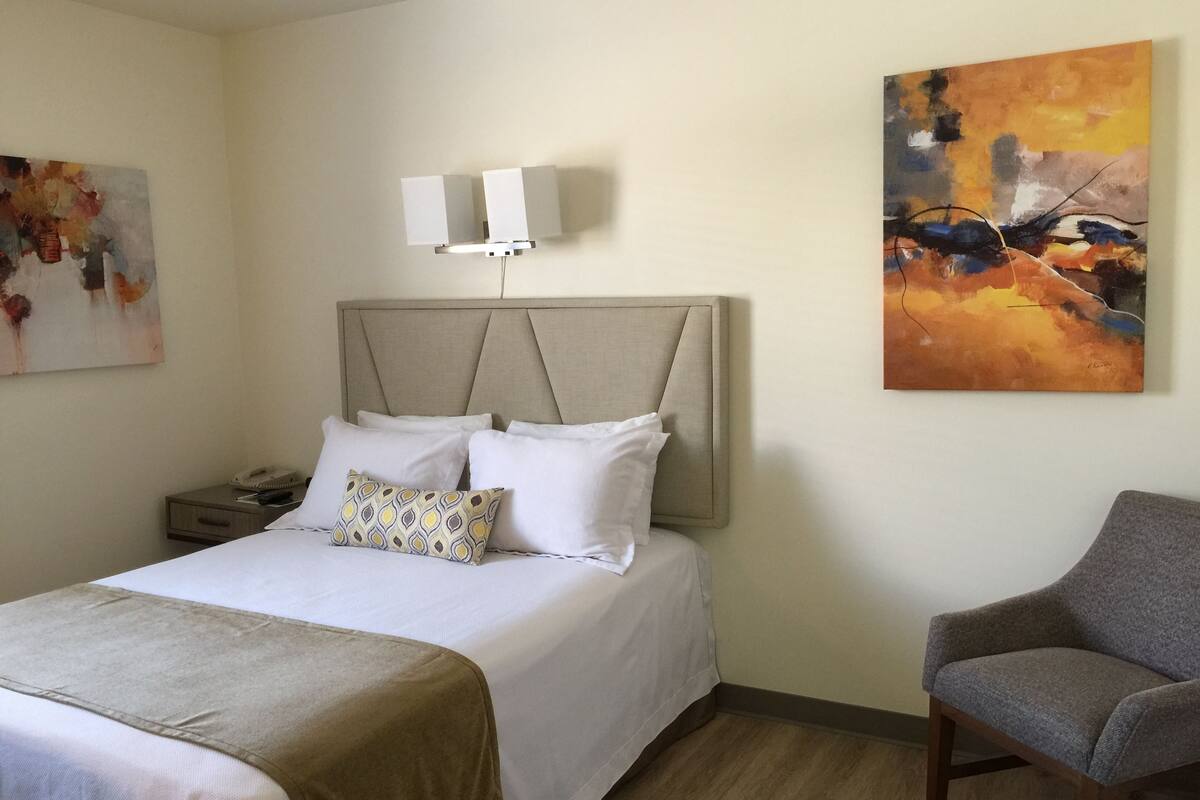 Een hotelkamer met een bed, nachtkastje, lamp en een stoel.