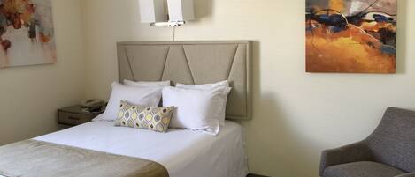 Ein Hotelzimmer mit Bett, Nachttisch, Lampe und einem Sessel.