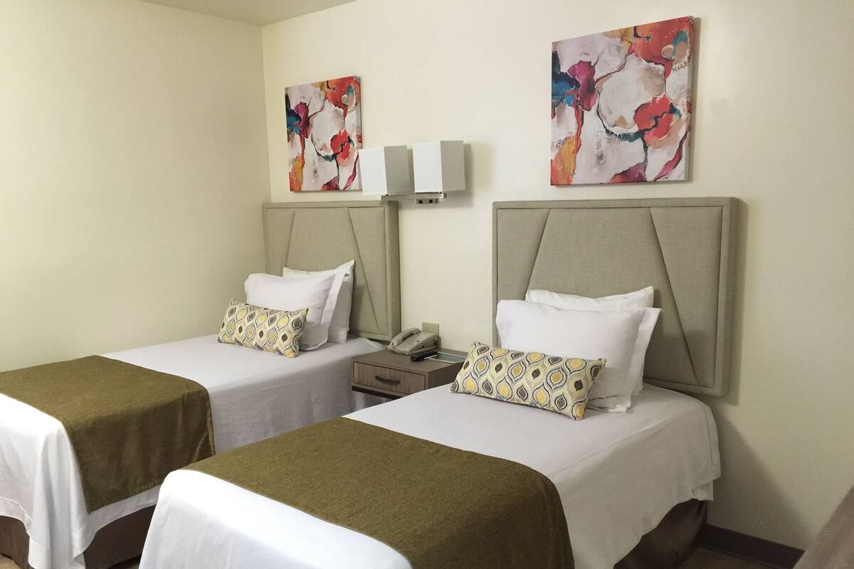 Een hotelkamer met twee eenpersoonsbedden, elk met hoofdbord, nachtkastje en telefoon. Boven de bedden hangen twee wandlampen.