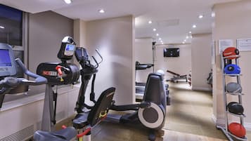 A gym with cardio machines, a weight bench, and a rack of dumbbells.