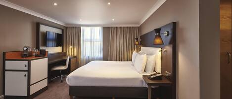 Habitación de hotel con cama, escritorio, silla, televisor, lámpara y teléfono.