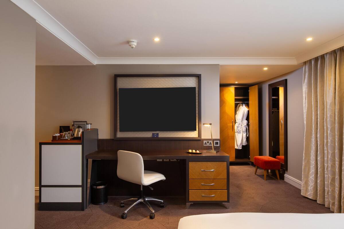A hotel room with a desk, chair, television, closet, and bathroom.