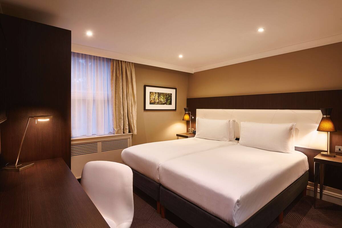A hotel room with a large bed, bedside lamps, a desk, and a chair.