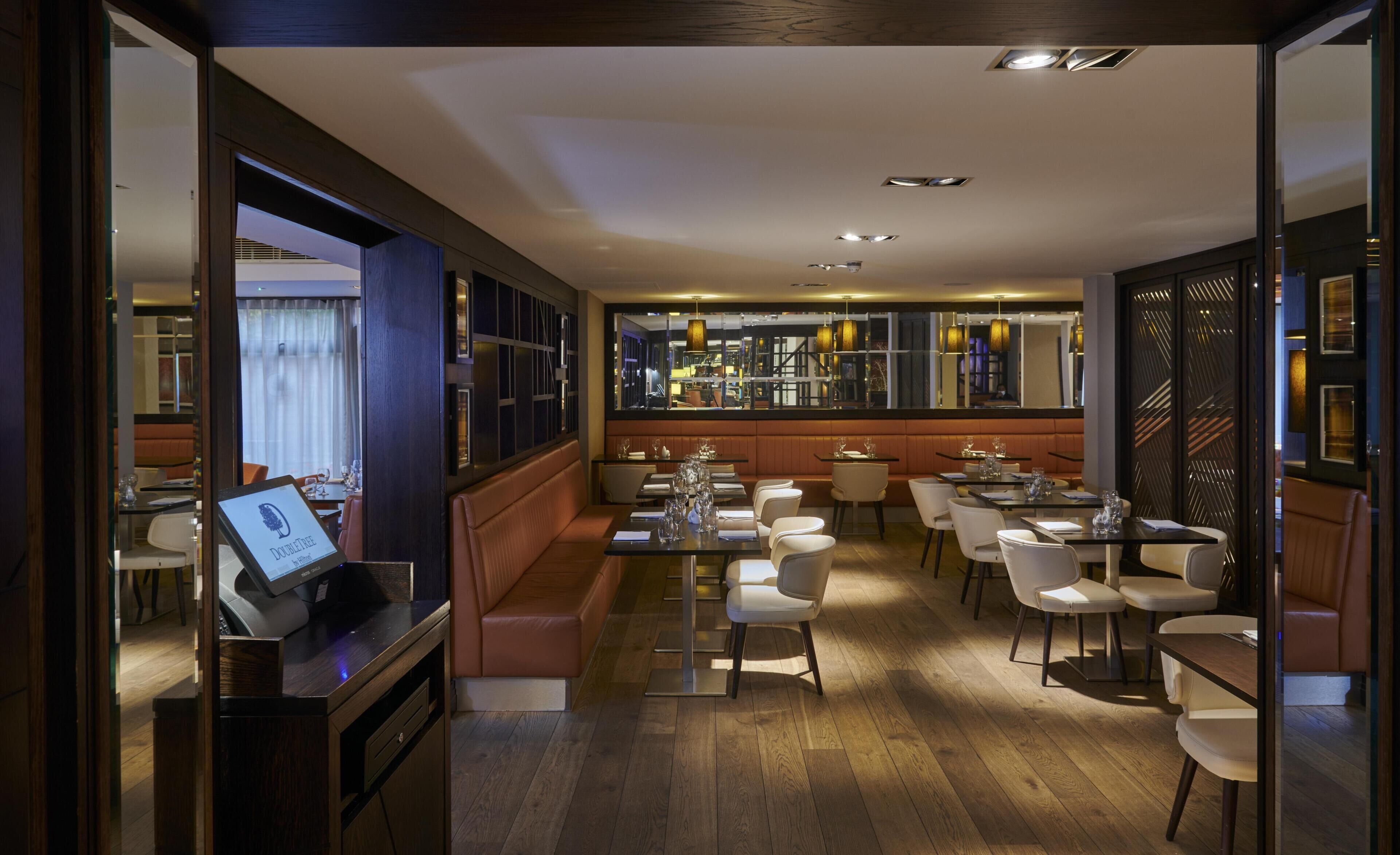 Restaurante com piso de madeira, cadeiras brancas e área de bar.