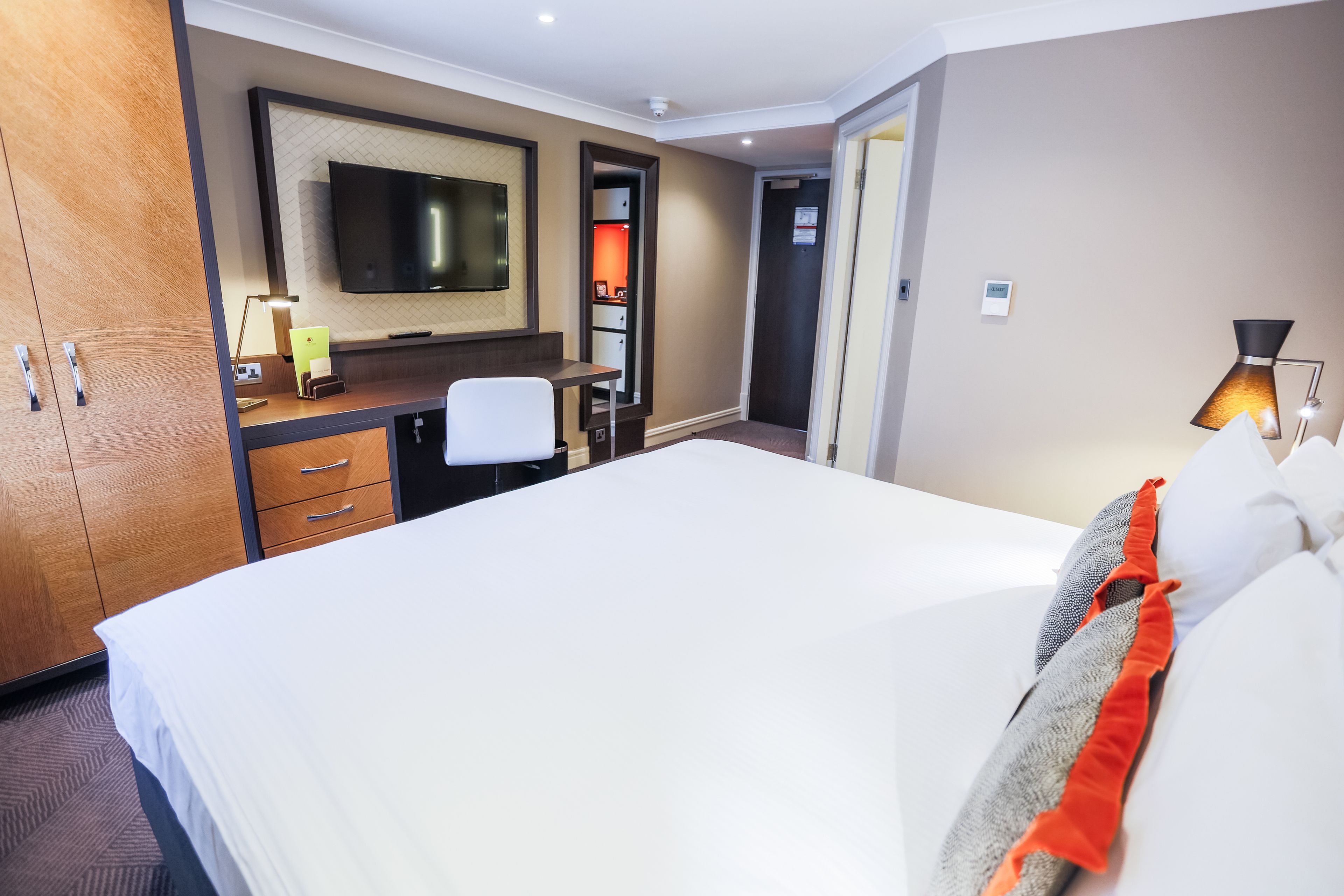 A hotel room with a large bed, a desk with a chair, a television, and a lamp.