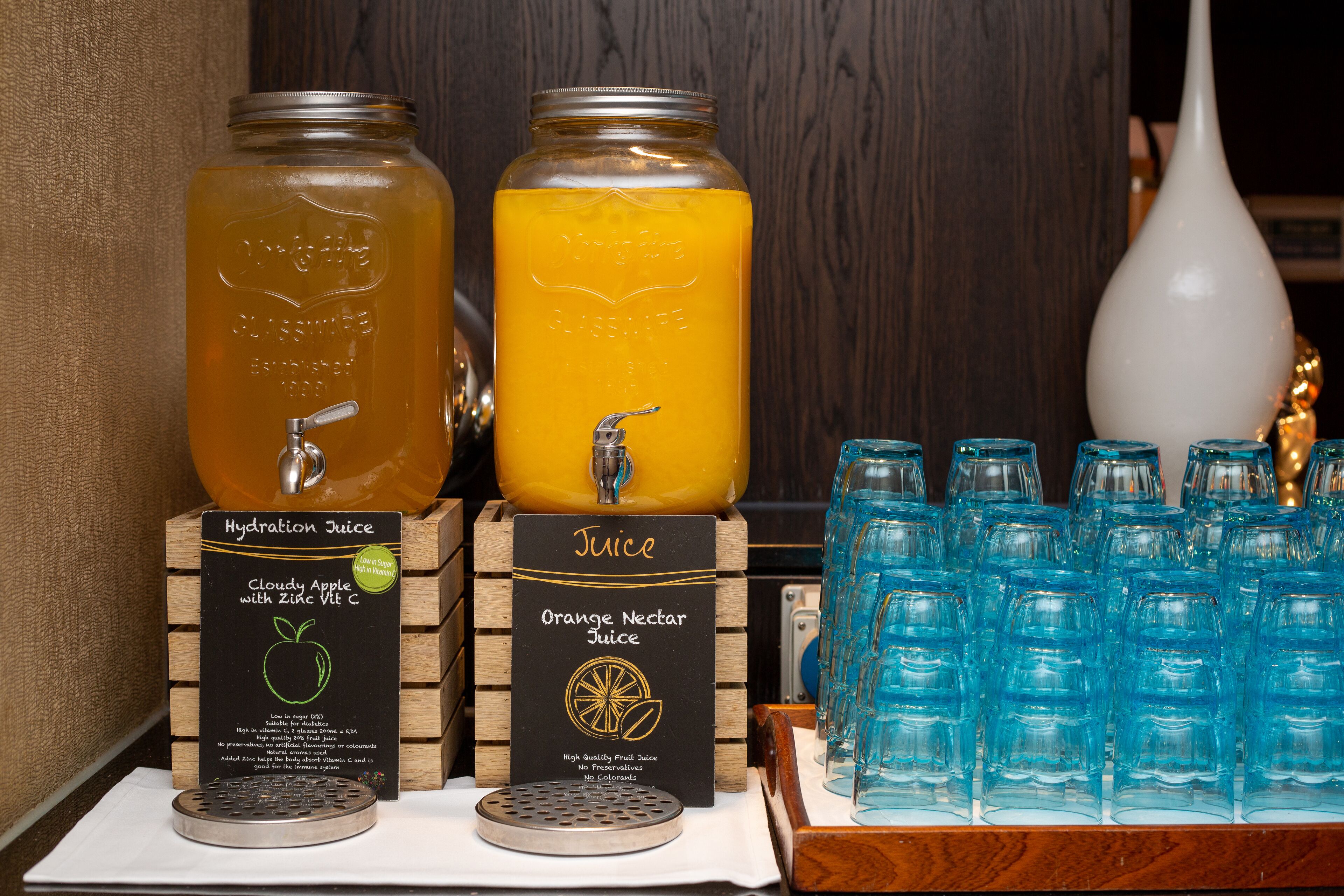 Two large glass jars labeled with different types of juice, a metal spout for dispensing, and a display of empty blue glass bottles.