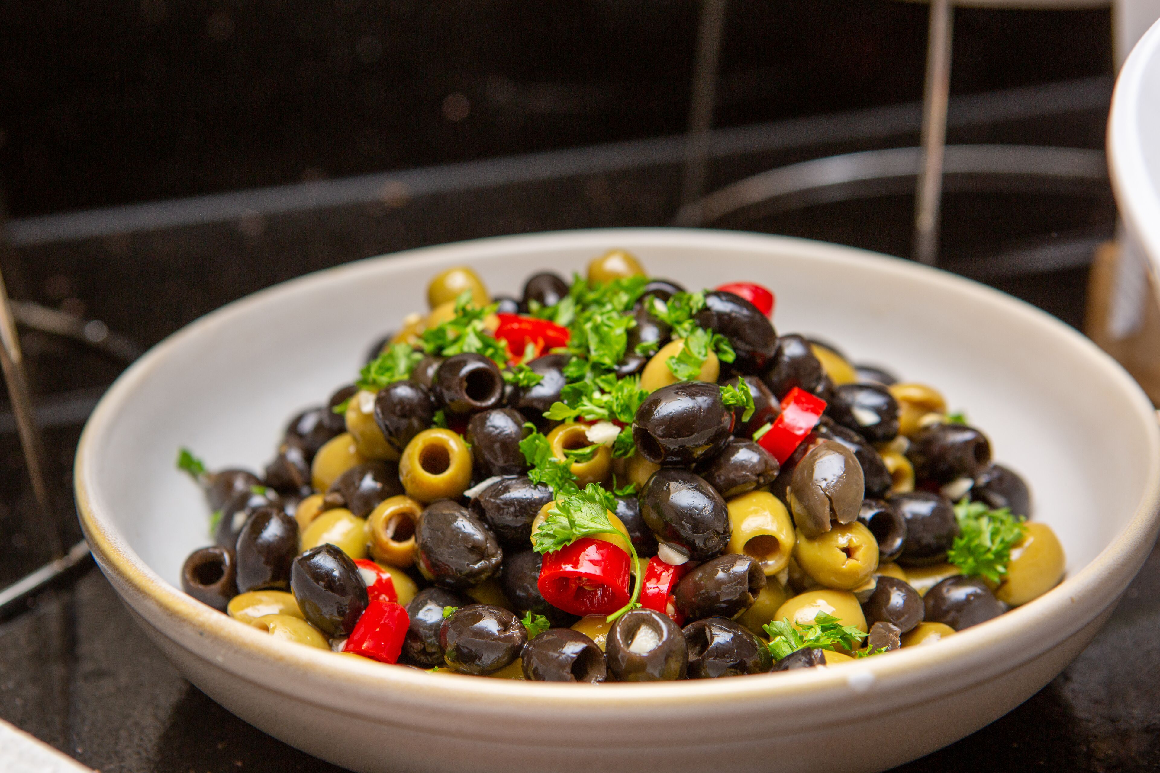 A bowl of olives with red peppers and parsley.