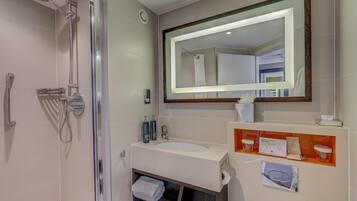 A modern bathroom with a shower, a large mirror, a sink, and a vanity with toiletries.