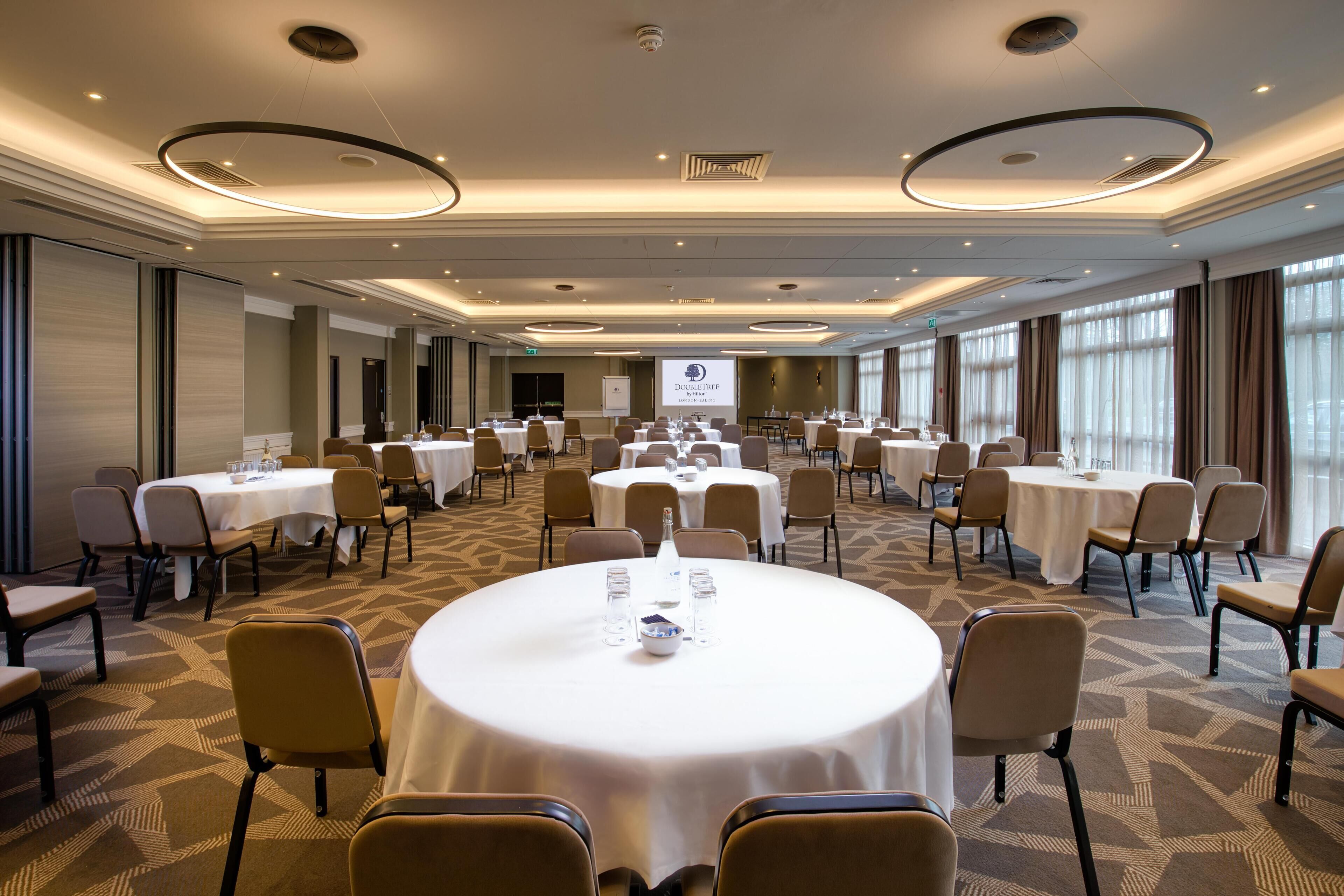 A conference room with round tables, chairs, and a projector screen.