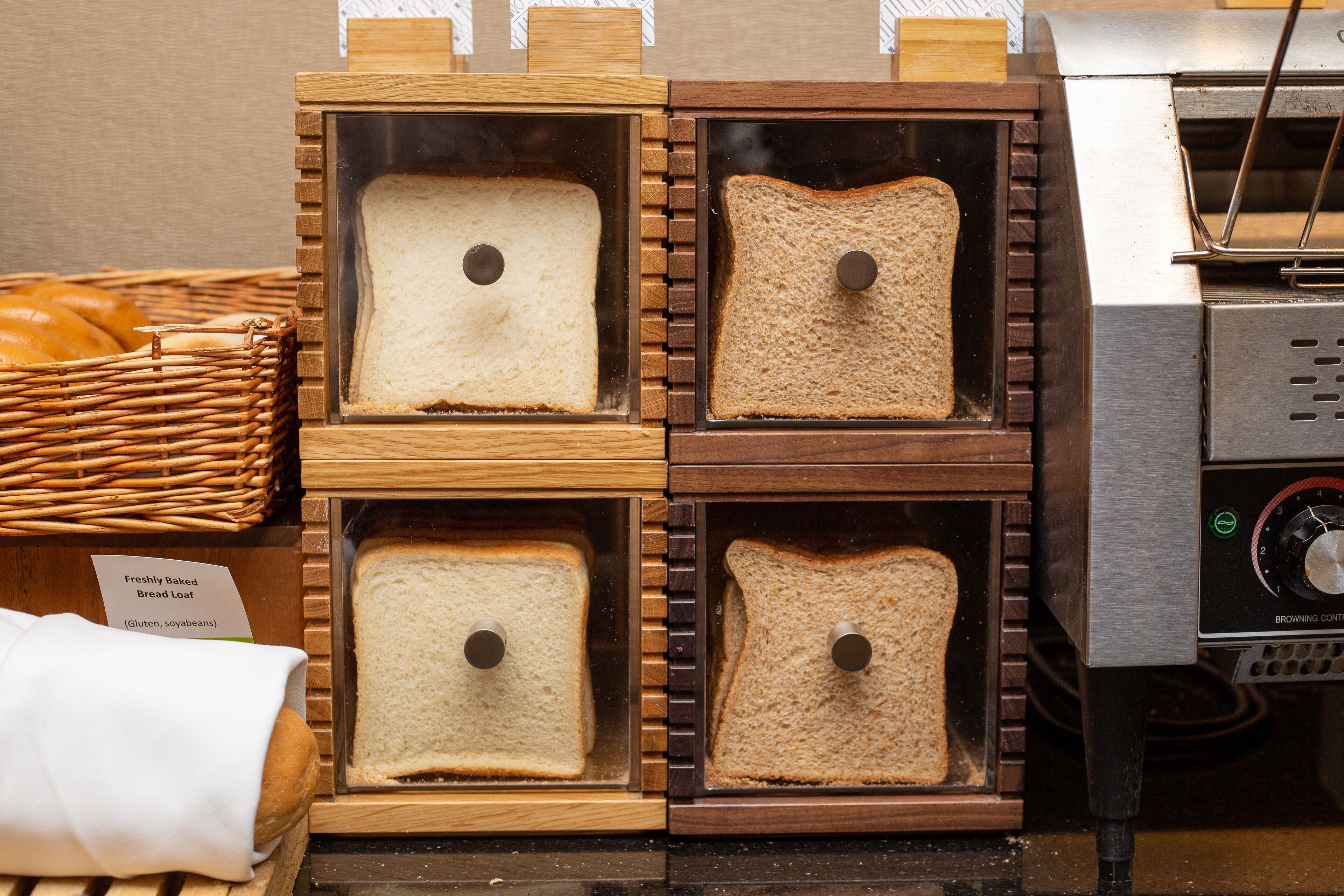 Four bread loaves in wooden boxes with a bread oven in the background.