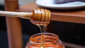 A honey dipper dripping honey into a glass jar.