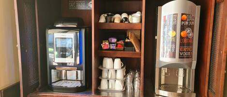 Un espace dédié au café, comprenant une machine à café, un distributeur de thé et une étagère avec des tasses et des condiments.