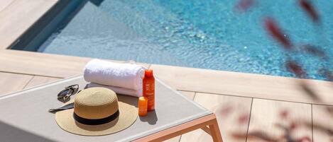 A poolside lounge chair with a sun hat, sunglasses, and sunscreen bottles.