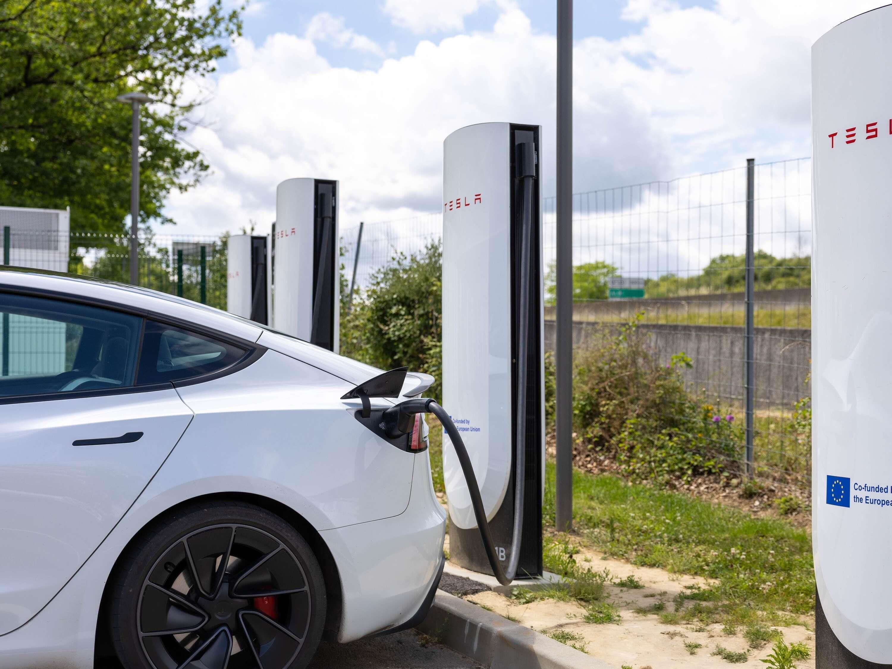 Een witte Tesla laadt op bij een laadstation met een logo van de Europese Unie.