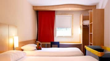 Quarto de hotel com duas camas, uma escrivaninha, uma cadeira, uma janela com cortina vermelha e um guarda-roupa.