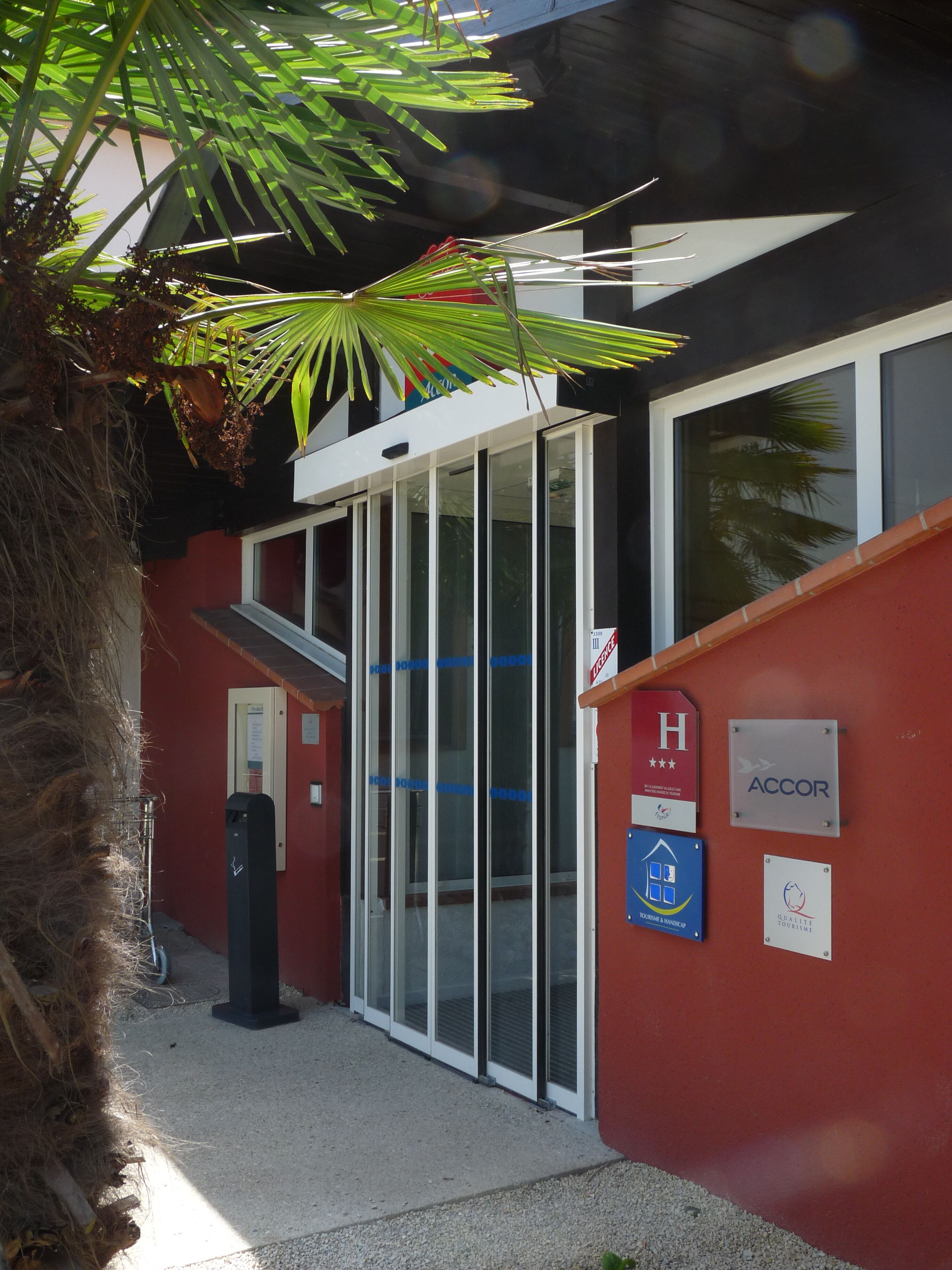 A hotel entrance with a glass door, ACCOR logo, and a sign indicating wheelchair accessibility.