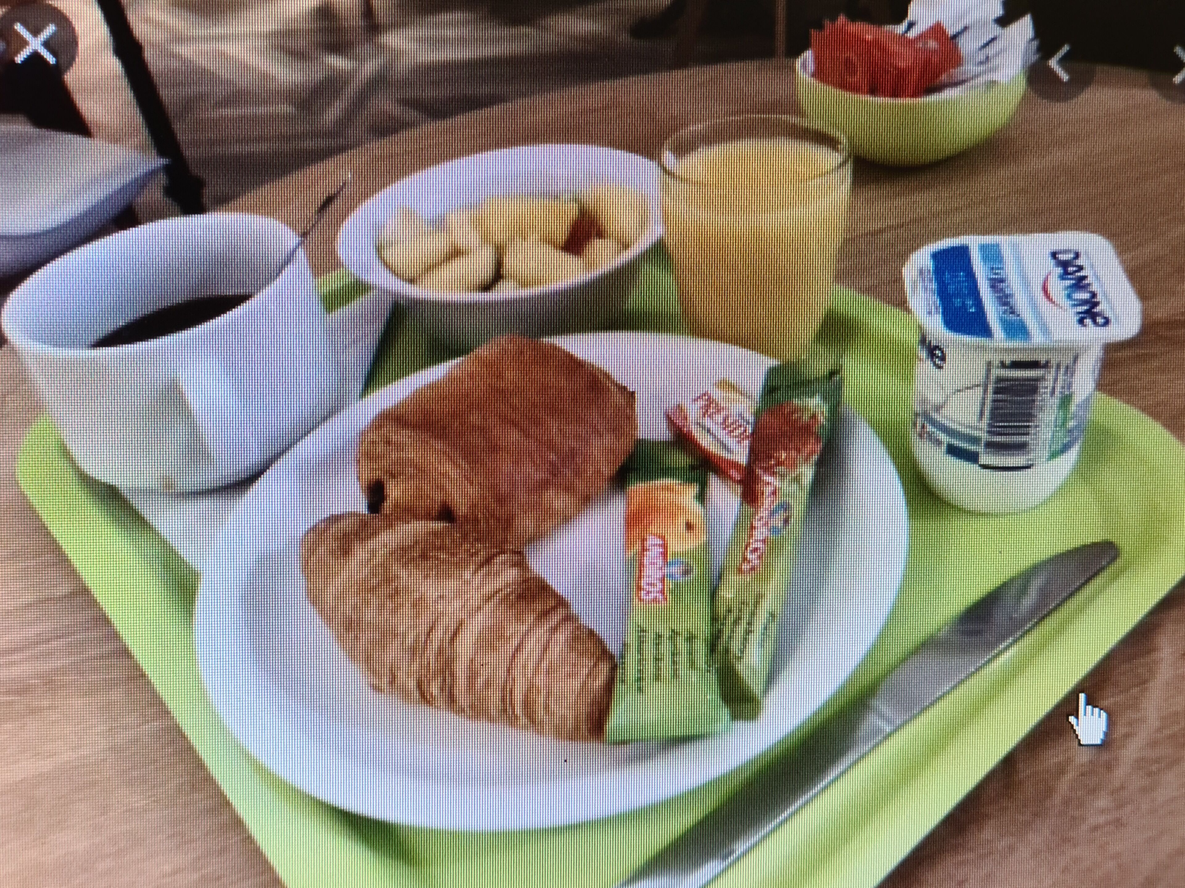 Mesa de café da manhã com croissants, uma tigela de frutas, um copo de suco e um pote de iogurte.