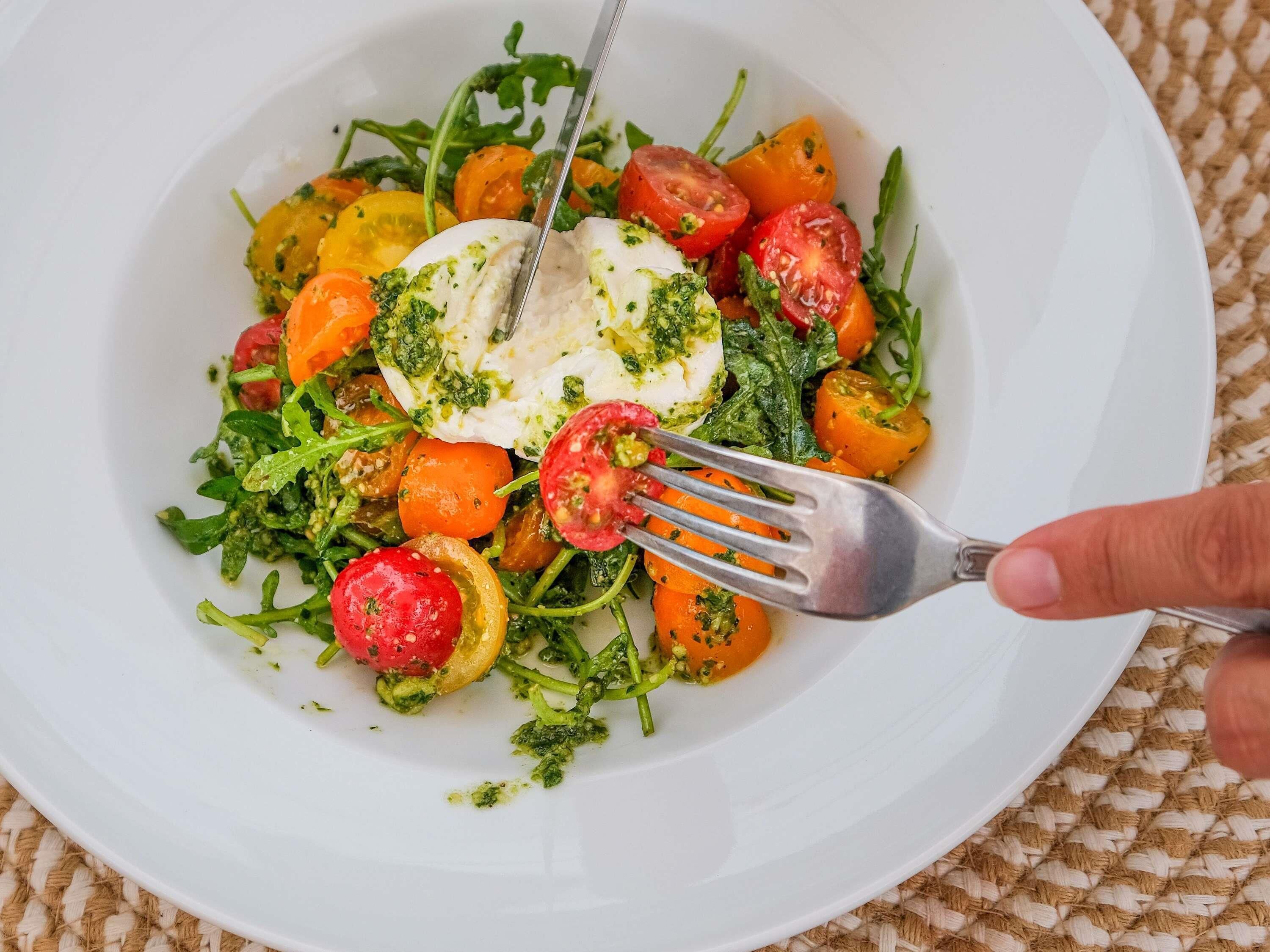 A white plate with a salad, including tomatoes, carrots, and a white item, possibly cheese or tofu, garnished with green herbs.