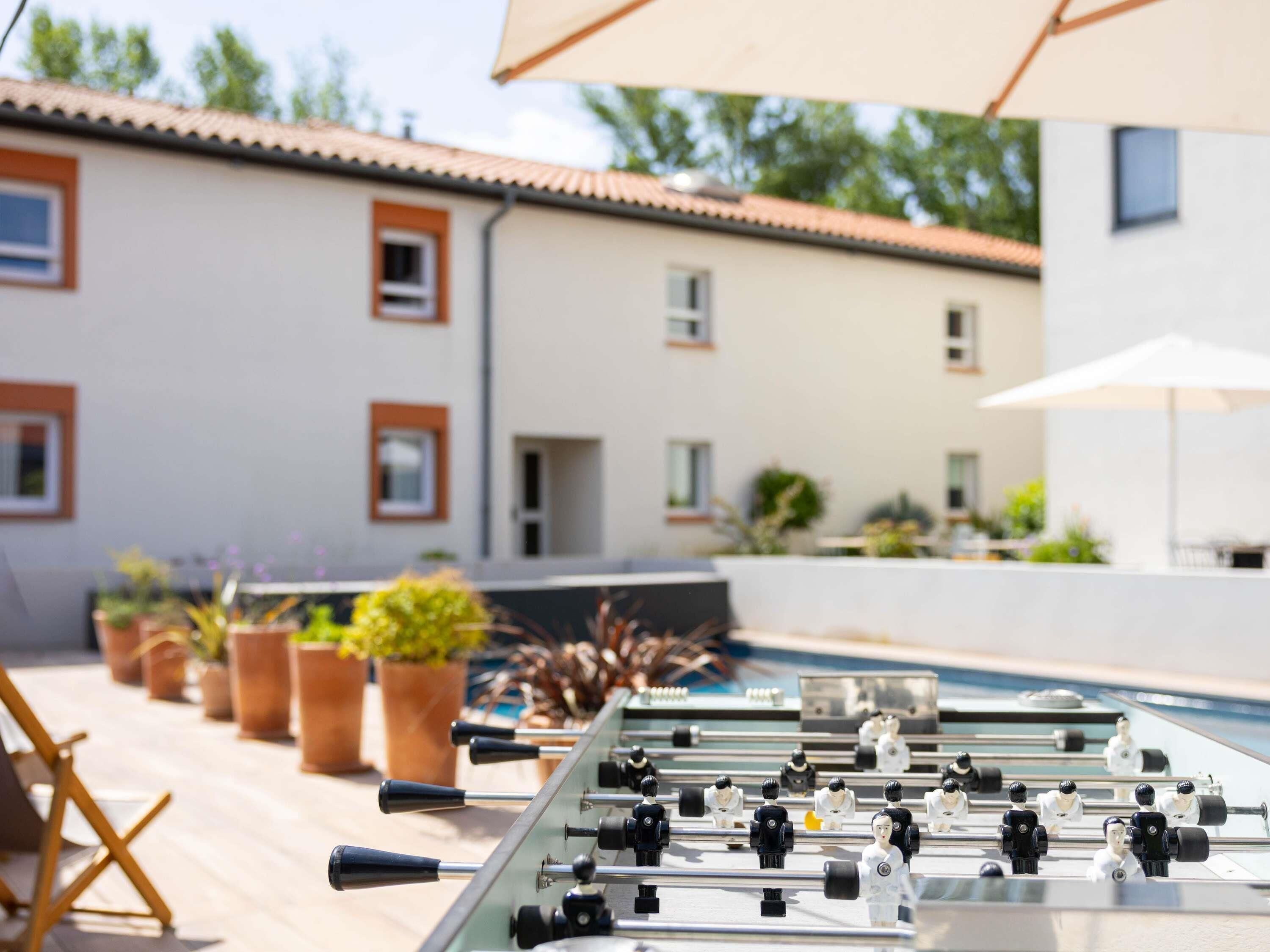 A foosball table in an outdoor area with potted plants and a building in the background.