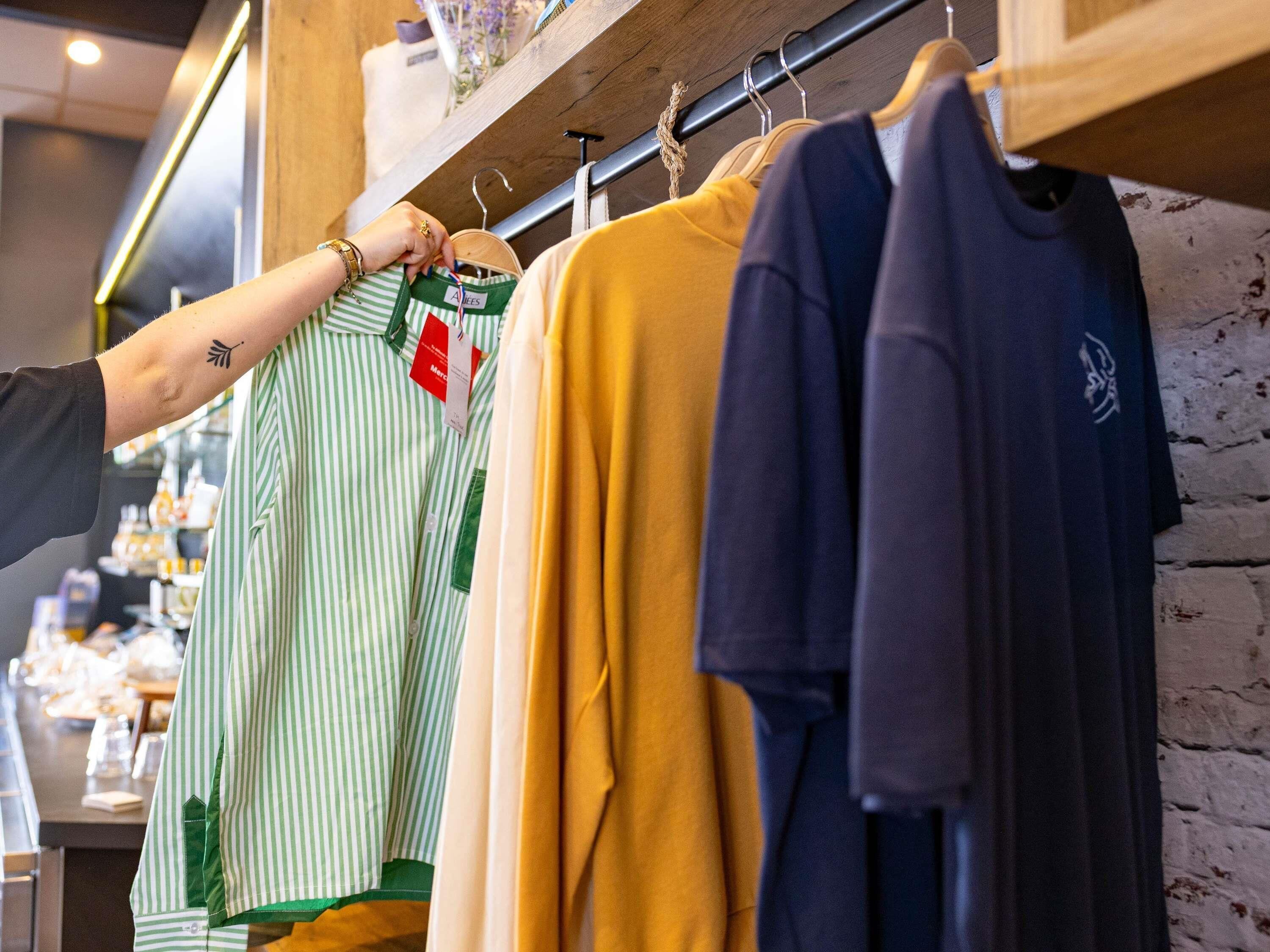 Un perchero con varias camisas, incluyendo una camisa verde a rayas y una camisa amarillo mostaza.