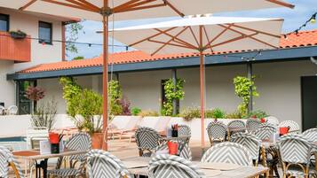 Un espace extérieur aménagé en terrasse, avec des chaises et des tables en osier, des parasols et des plantes en pot.