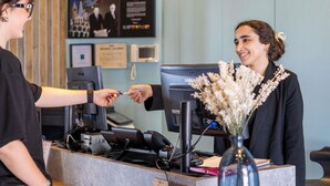 Una reception con uno schermo Samsung, un telefono e una cassa. Si nota un certificato incorniciato al muro e un vaso con fiori sul bancone.