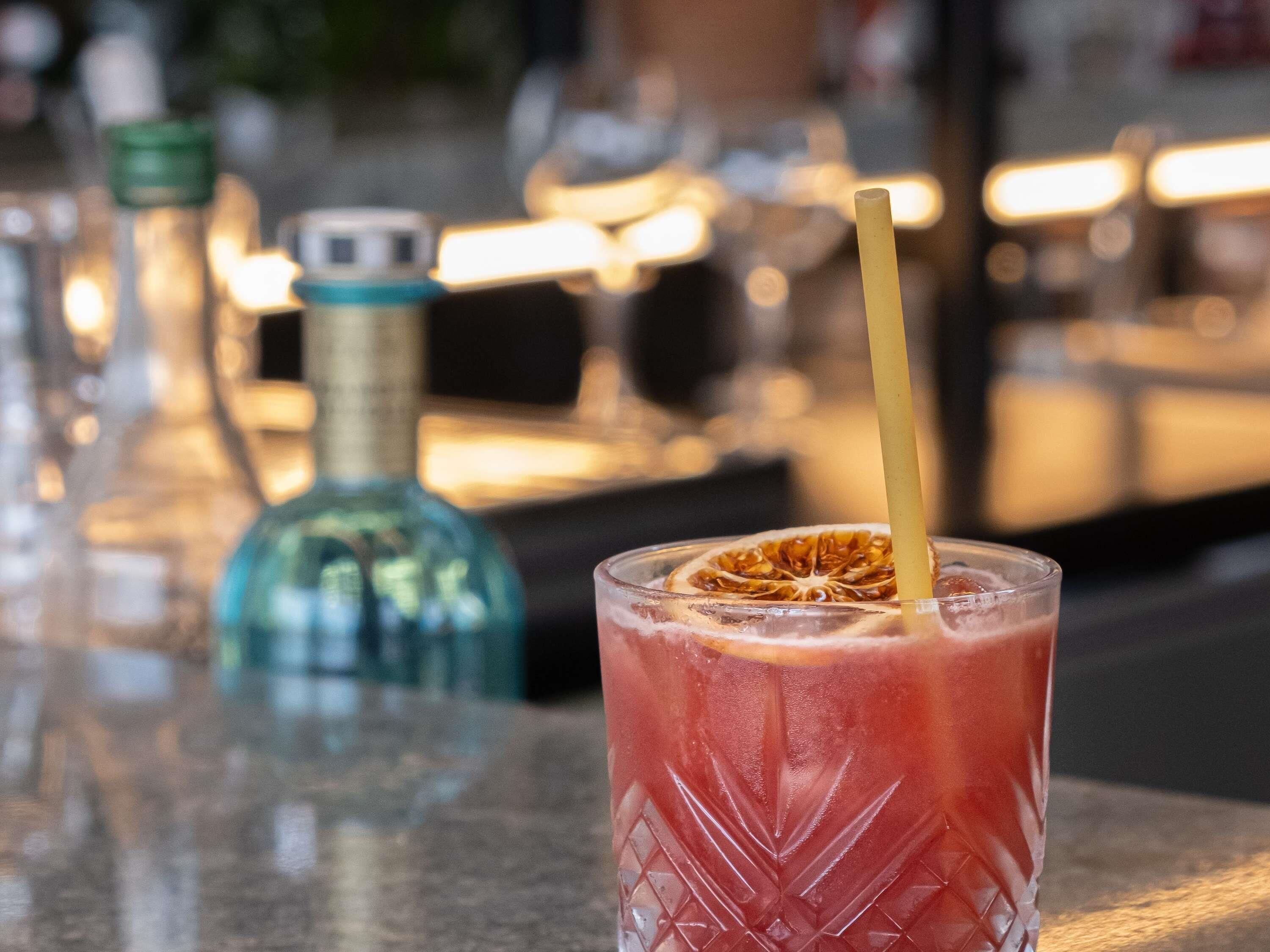 Une scène de bar avec un verre d’une boisson rouge et une bouteille en arrière-plan.