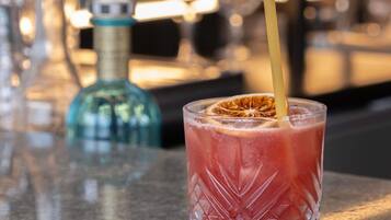 Une scène de bar avec un verre d’une boisson rouge et une bouteille en arrière-plan.