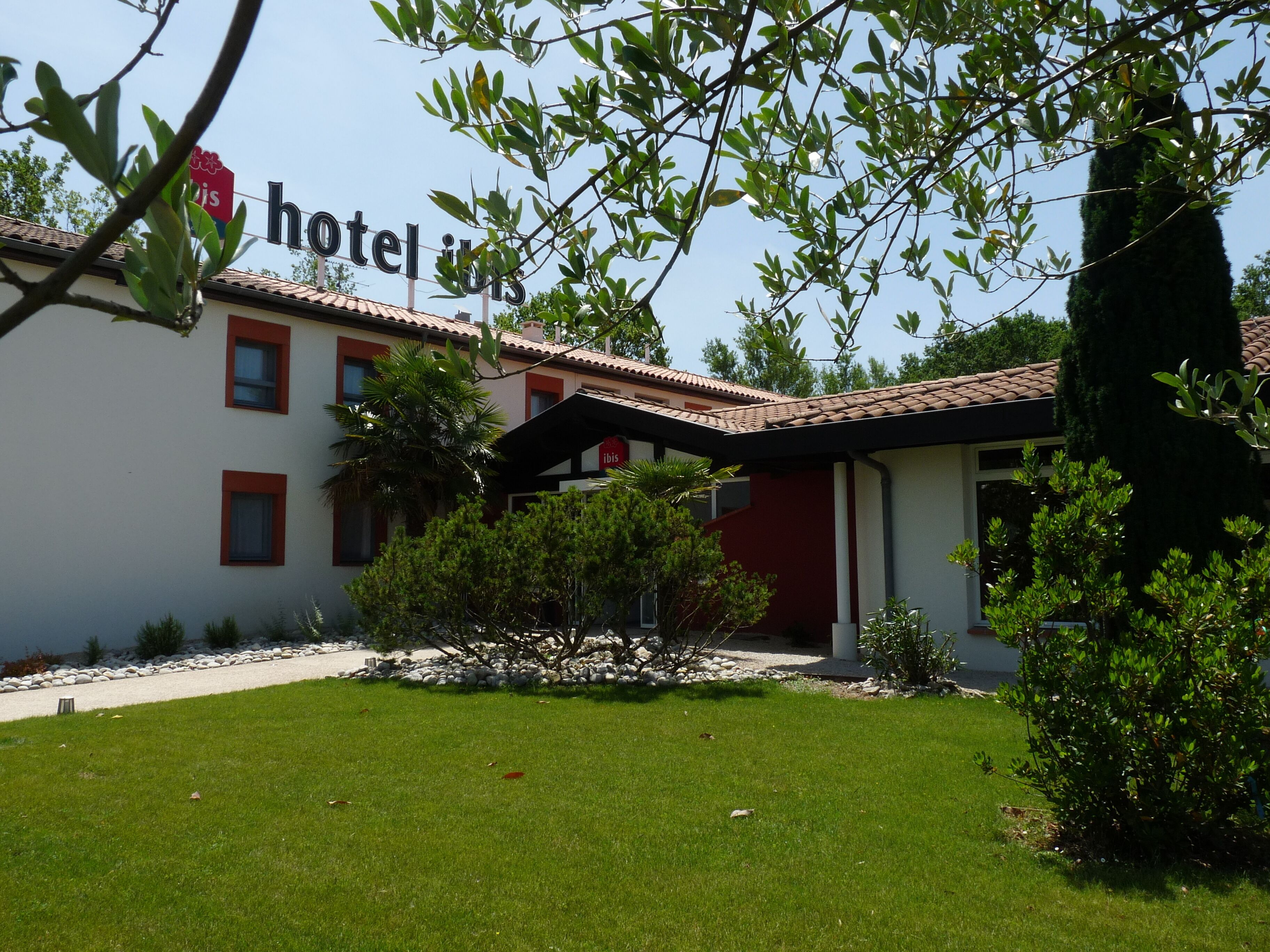 Un hotel amb façana vermella i blanca, teulada d'àmples rajoles i un jardí ben cuidat.