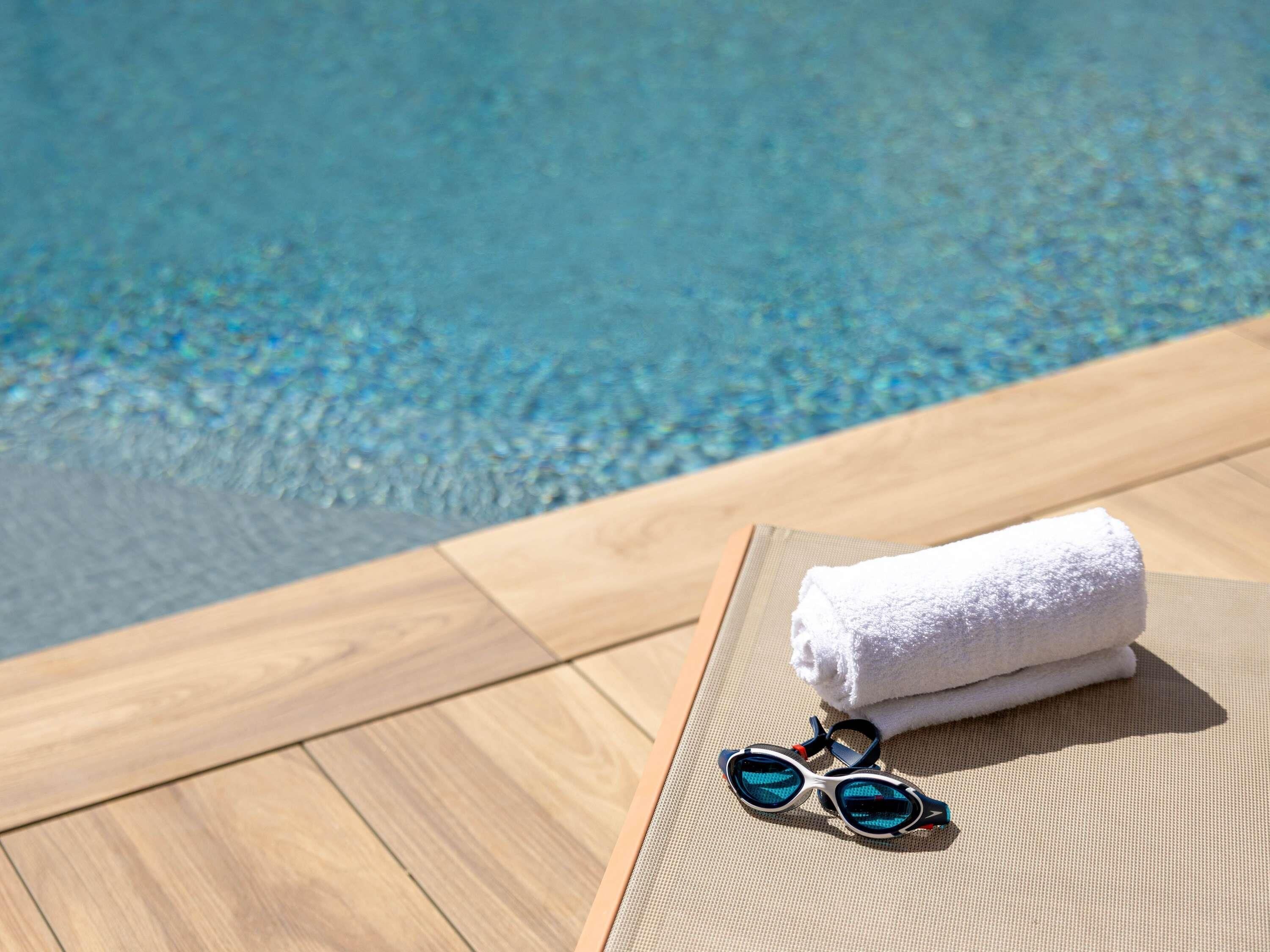 A poolside area with a wooden deck, a white towel, and swimming goggles.