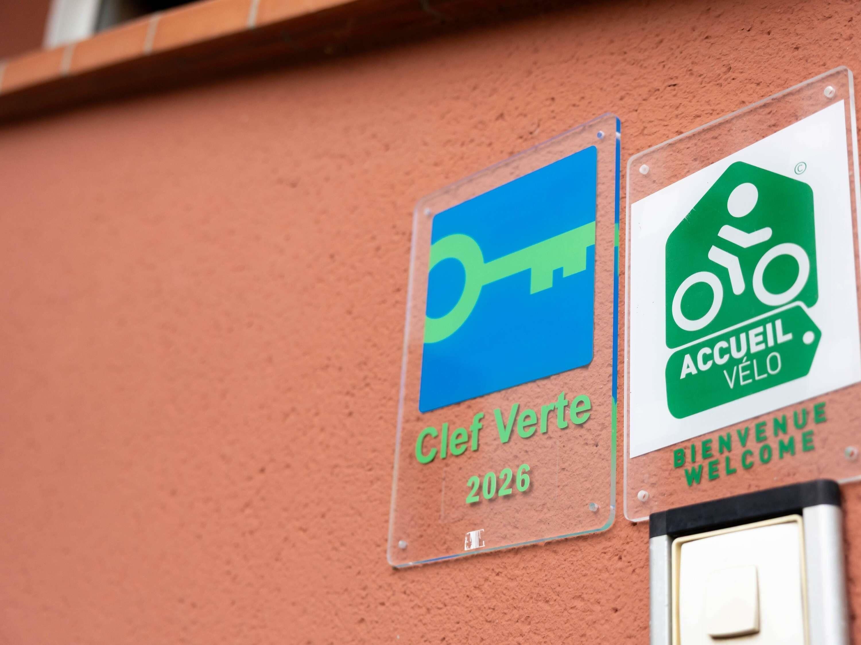 Dos letreros en una pared: uno con el símbolo de una llave y el texto 'Cler Verde 2026', y otro con el símbolo de una bicicleta y el texto 'Accueil Vélo'.