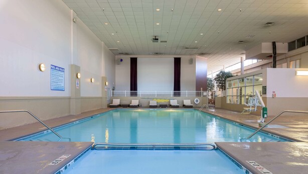 Una piscina interior con agua cristalina, un cartel de normas para la zona de la piscina y una barandilla blanca alrededor.