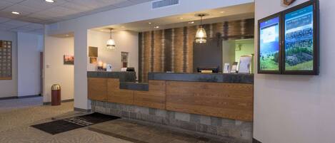 A reception area with a wooden counter, a clock, and a digital display showing weather information.