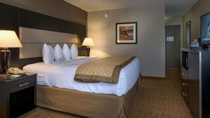 Habitación de hotel con una cama, dos lámparas de noche, una mesita de noche, un escritorio con lámpara, un televisor y un cuadro en la pared.