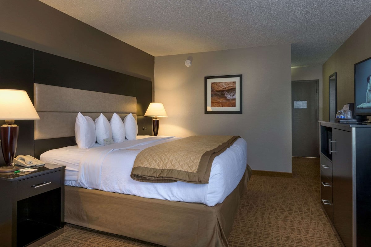 A hotel room with a bed, two bedside lamps, a nightstand, a desk with a lamp, a television, and a framed picture on the wall.