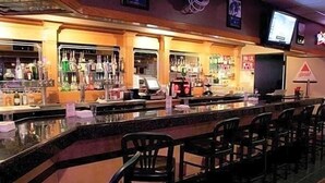 Una zona de bar con mostrador, taburetes y estantes llenos de botellas.