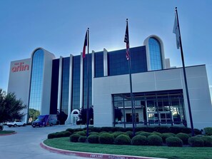 Un edificio moderno con una amplia entrada arqueada, varias banderas y cielo despejado.