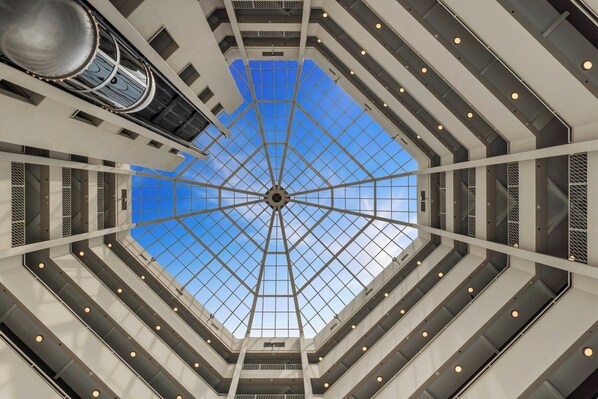 A modern atrium with a glass ceiling, multiple levels, and a central elevator shaft. - The Arlin, Arlington, a Tribute Portfolio Hotel (Arlington)