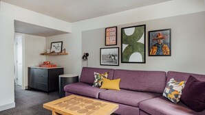 Un salon moderne avec un canapé violet, une table basse en bois et des œuvres d’art accrochées aux murs.