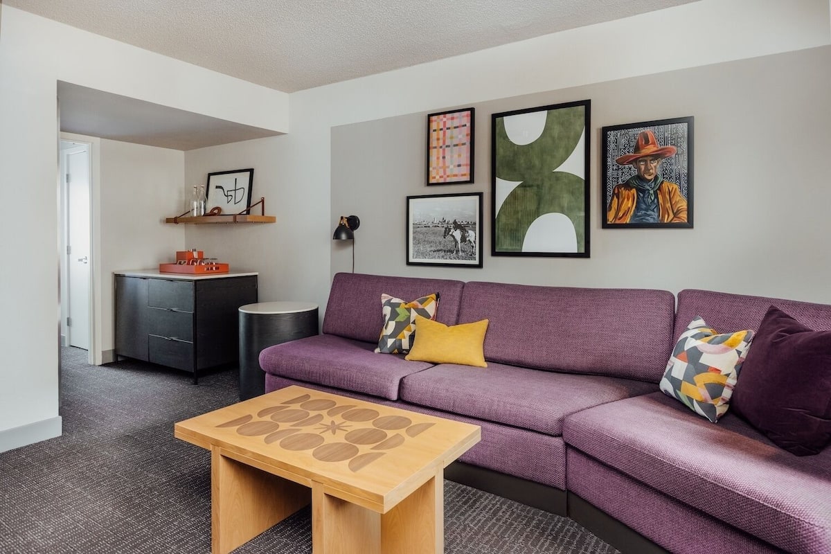 A modern living room with a purple sofa, a wooden coffee table, and artwork on the walls.