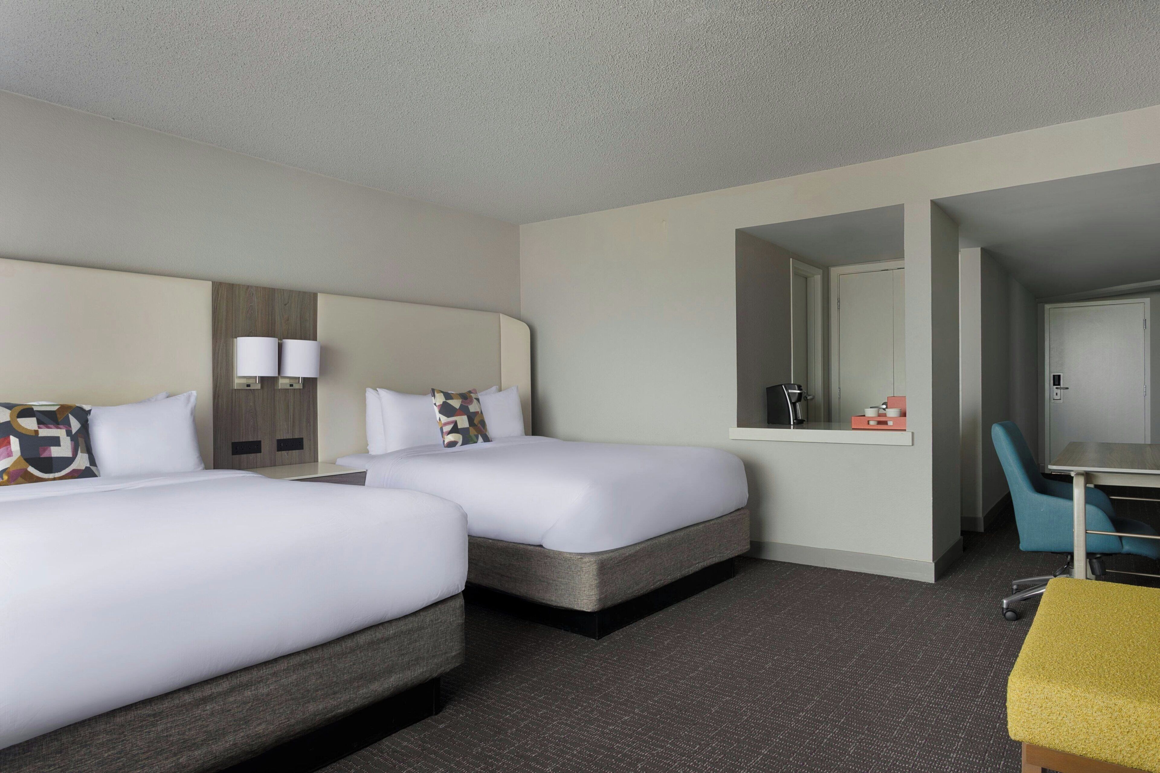 Une chambre d’hôtel avec deux lits, un bureau, une chaise et un miroir.