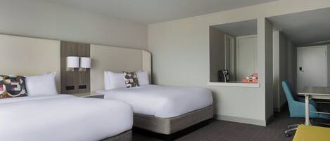 A hotel room with two beds, a desk, a chair, and a mirror.