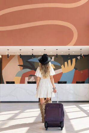 Una persona con maleta en un vestíbulo moderno con arte abstracto en la pared y una mesa de recepción.