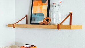 A kitchen counter with a wooden shelf holding a framed picture, two glass bottles, and a wicker basket. Below the shelf, there's an orange tray with glass jars and a card. - The Arlin, Arlington, a Tribute Portfolio Hotel (Arlington)