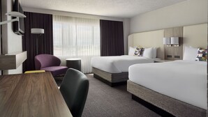 Une chambre d’hôtel avec deux lits, un bureau, une chaise, une télévision et une fenêtre avec des rideaux.