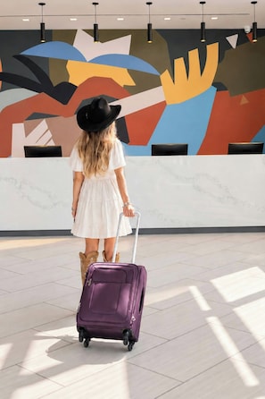 A person with a purple suitcase in a lobby with a modern geometric wall design.