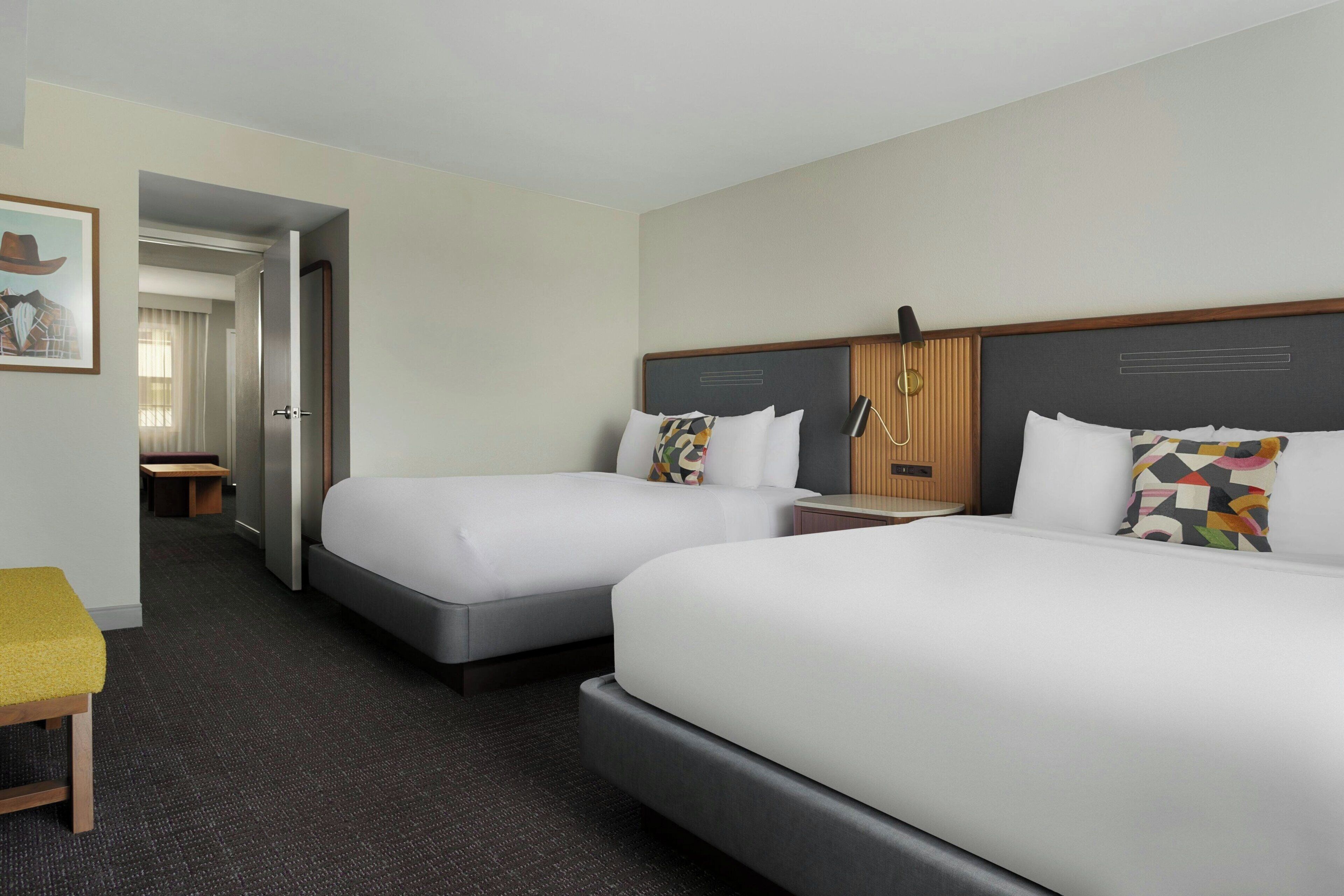 Habitación de hotel con dos camas, un escritorio, una silla y una puerta que da a otra habitación.