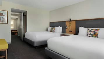 Habitación de hotel con dos camas, un escritorio, una silla y una puerta que da a otra habitación.