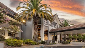 A modern hotel with a palm tree in the foreground, a parking lot, and a sunset sky. - Best Western Plus Novato Oaks Inn (Novato)