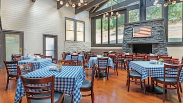 A restaurant with multiple tables covered with blue and white checkered tablecloths, wooden chairs, and a stone fireplace with an American flag.